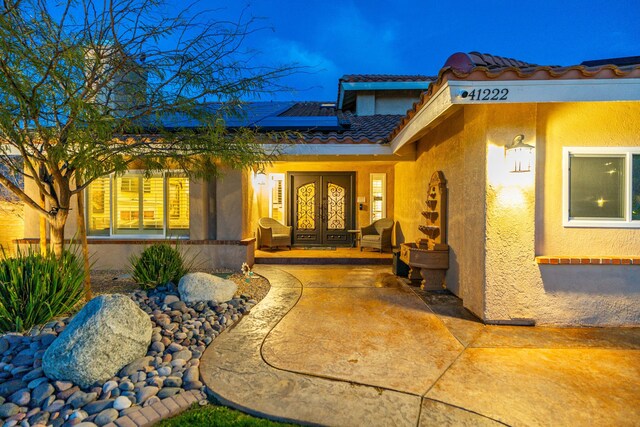 view of exterior entry with solar panels, french doors, a tiled roof, and stucco siding