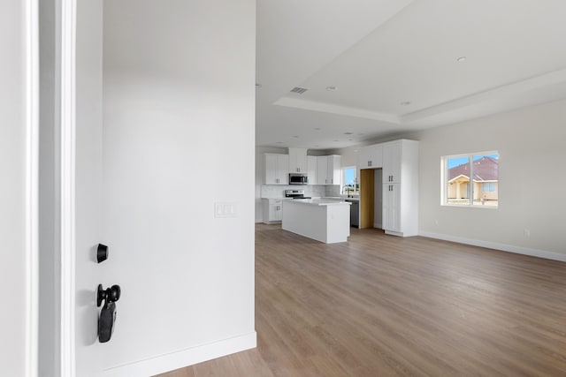 interior space featuring a raised ceiling, light wood-style flooring, and baseboards