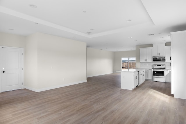 kitchen with light wood-type flooring, light countertops, appliances with stainless steel finishes, a raised ceiling, and open floor plan