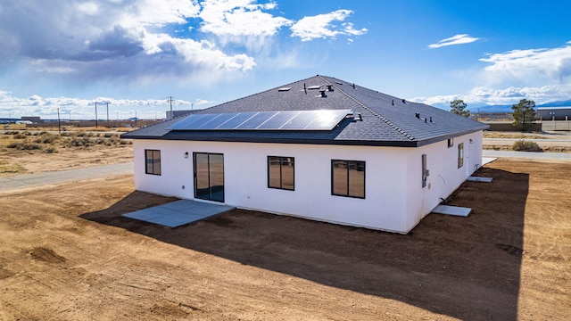 rear view of house with a patio area, roof mounted solar panels, and a shingled roof