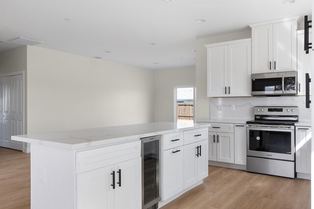 kitchen featuring beverage cooler, decorative backsplash, appliances with stainless steel finishes, light wood-style floors, and white cabinets