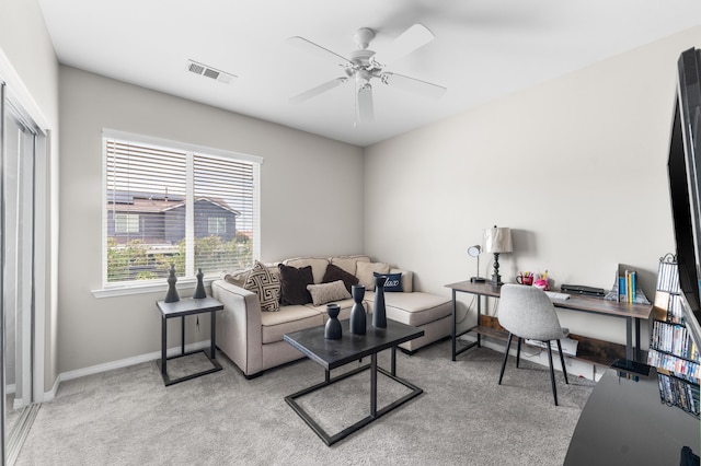 living room featuring ceiling fan, a desk, baseboards, and light colored carpet