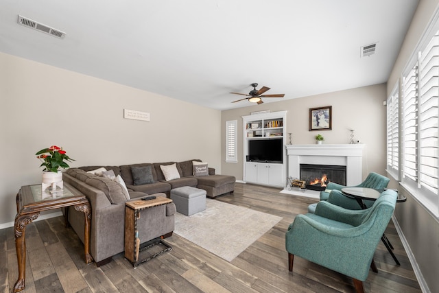 living area featuring ceiling fan, wood finished floors, a fireplace with flush hearth, and baseboards