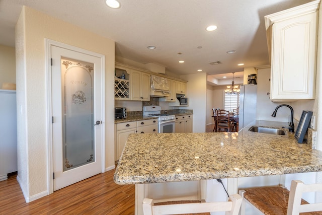 kitchen featuring a breakfast bar area, kitchen peninsula, sink, and white appliances