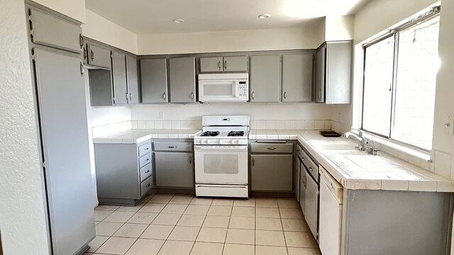 kitchen with white appliances, tile countertops, gray cabinets, and sink