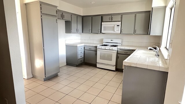 kitchen with white appliances, sink, gray cabinets, light tile patterned floors, and tile counters