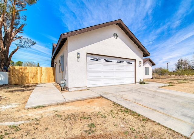 view of side of home featuring driveway, stucco siding, and fence