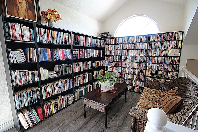 sitting room with bookshelves, lofted ceiling, a textured wall, and wood finished floors