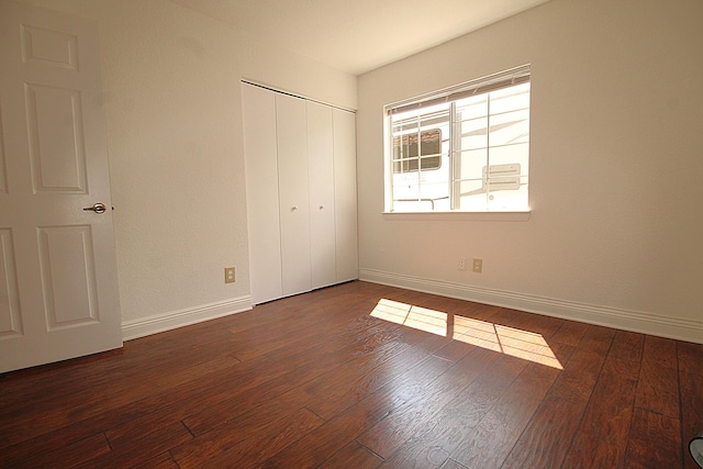 unfurnished bedroom featuring baseboards, a closet, and dark wood-type flooring