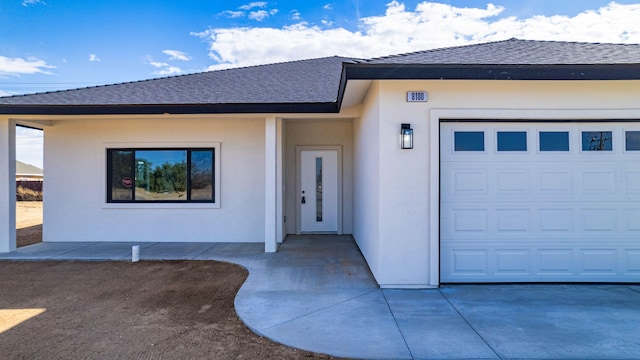 view of front of home with stucco siding, a garage, and roof with shingles