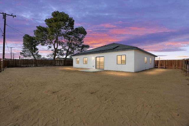 back of house at dusk featuring solar panels, a patio area, a fenced backyard, and stucco siding