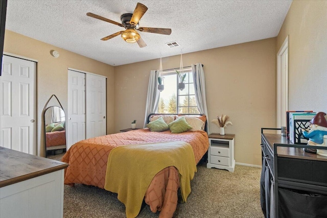 carpeted bedroom featuring ceiling fan, a textured ceiling, and multiple closets