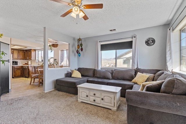 carpeted living room featuring ceiling fan and a textured ceiling