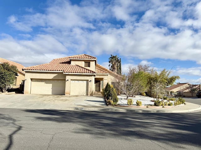 mediterranean / spanish house with a garage, a tiled roof, concrete driveway, and stucco siding