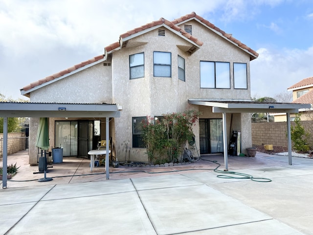 back of house with a tile roof, a patio, fence, and stucco siding