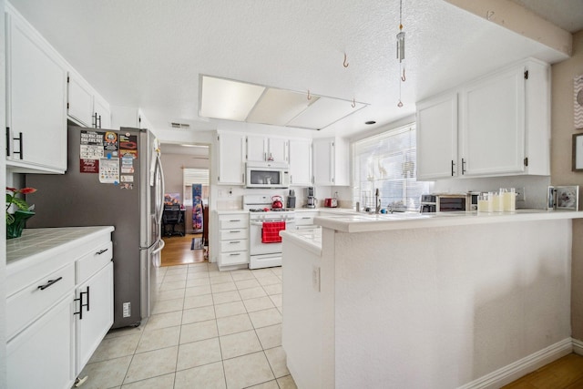 kitchen featuring light tile patterned floors, light countertops, white cabinetry, white appliances, and a peninsula