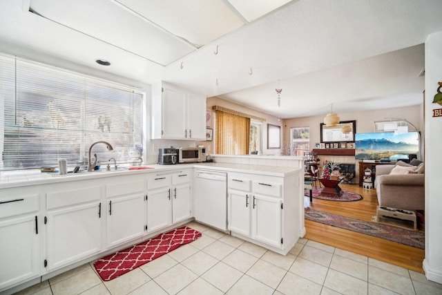 kitchen featuring stainless steel microwave, white cabinetry, white dishwasher, a sink, and a peninsula