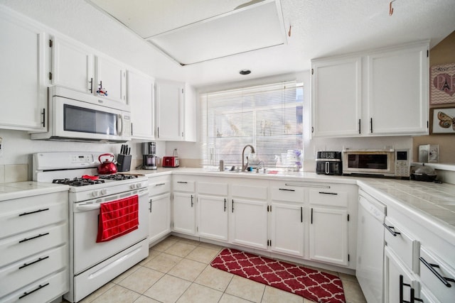 kitchen featuring white appliances, white cabinetry, a sink, and light tile patterned flooring