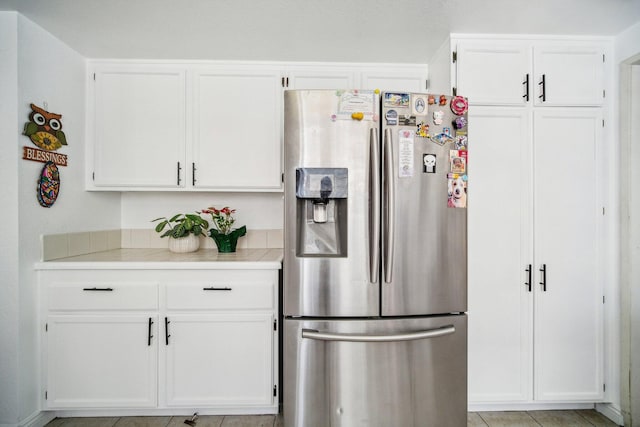 kitchen featuring light tile patterned flooring, stainless steel refrigerator with ice dispenser, and white cabinetry