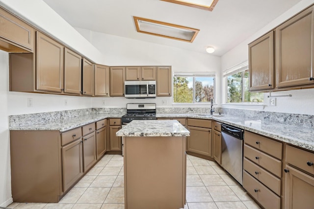 kitchen featuring light stone countertops, a sink, a center island, stainless steel appliances, and vaulted ceiling