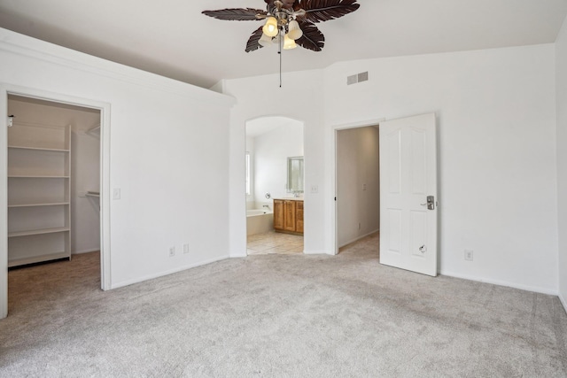 unfurnished bedroom with a walk in closet, visible vents, arched walkways, light carpet, and ensuite bath