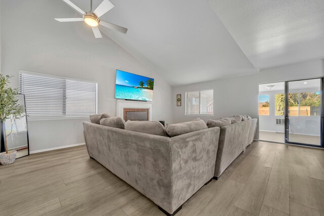 living room featuring a fireplace, light hardwood / wood-style floors, vaulted ceiling, and ceiling fan