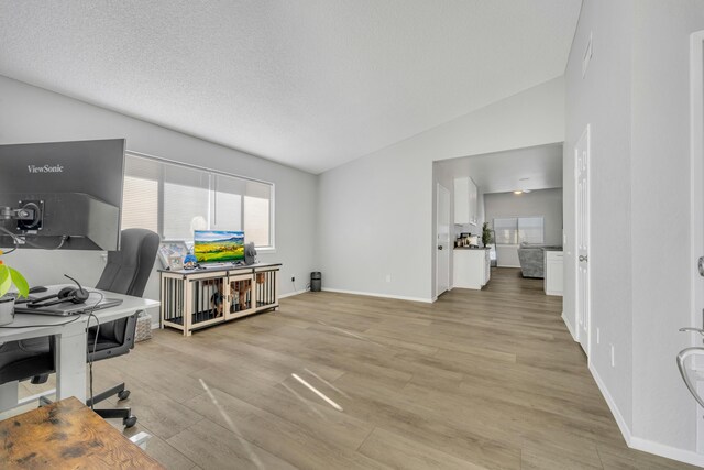 office area with a textured ceiling, vaulted ceiling, and light hardwood / wood-style flooring