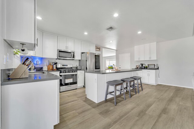 kitchen with a kitchen island, light hardwood / wood-style floors, a kitchen bar, white cabinets, and appliances with stainless steel finishes