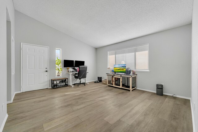 office area featuring lofted ceiling, light wood-type flooring, and a textured ceiling