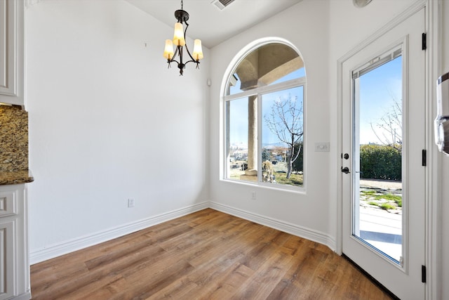 unfurnished dining area with a notable chandelier, plenty of natural light, and light hardwood / wood-style flooring