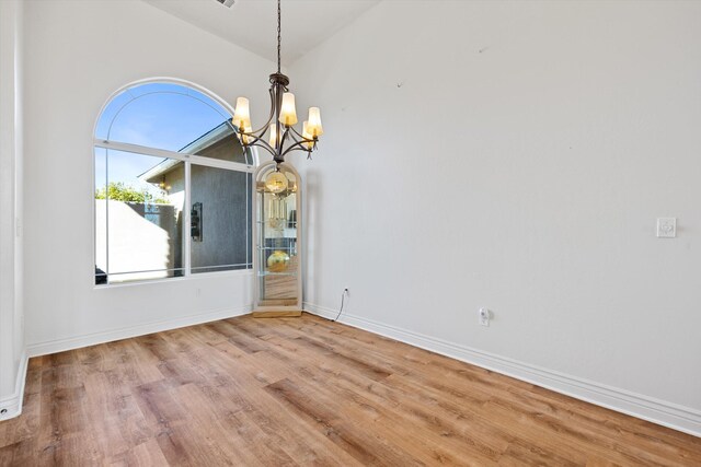 unfurnished dining area with hardwood / wood-style floors, lofted ceiling, and a chandelier