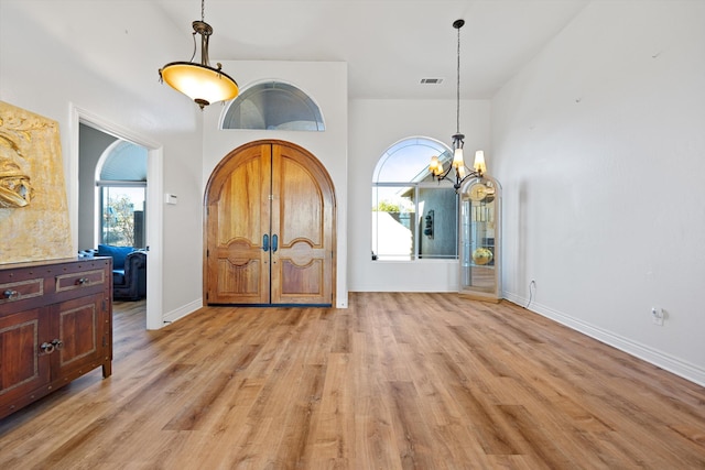 foyer entrance with light wood-type flooring, a high ceiling, and an inviting chandelier