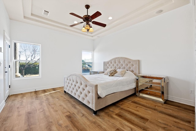 bedroom featuring a raised ceiling, ceiling fan, and wood-type flooring