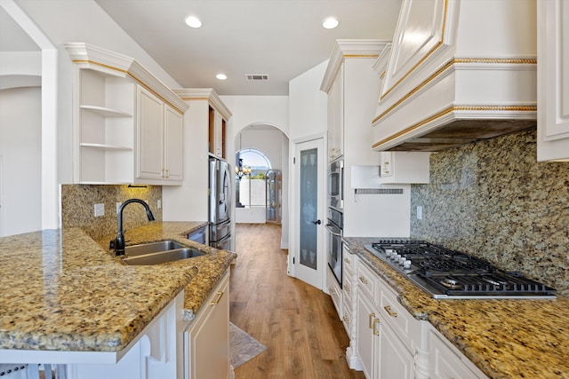 kitchen with appliances with stainless steel finishes, premium range hood, sink, stone counters, and white cabinetry