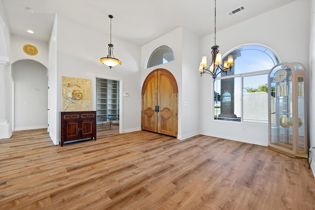 entryway with light hardwood / wood-style flooring, a towering ceiling, and an inviting chandelier