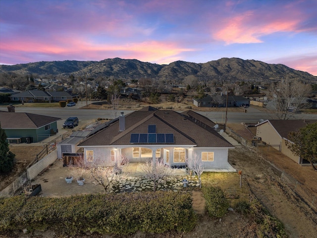 back house at dusk with a mountain view and solar panels