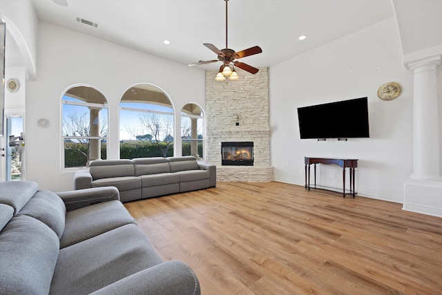 living room featuring decorative columns, ceiling fan, a fireplace, and light hardwood / wood-style floors