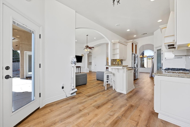 kitchen with a kitchen bar, ceiling fan, white cabinets, and light stone countertops