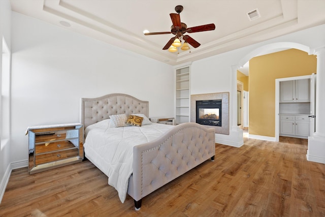 bedroom with ceiling fan, a raised ceiling, a fireplace, and light hardwood / wood-style flooring