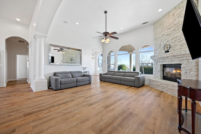 living room with ceiling fan, a fireplace, light hardwood / wood-style floors, and a high ceiling