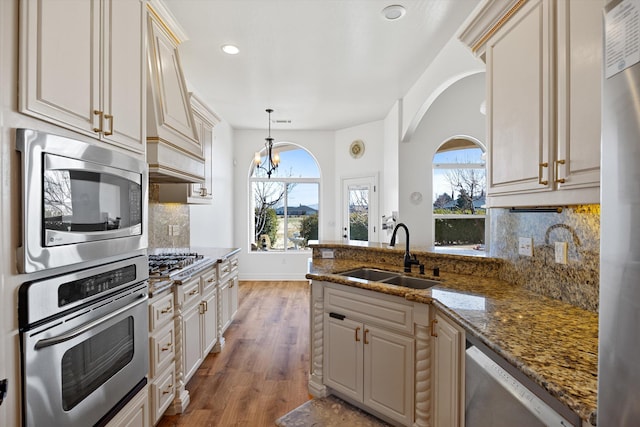 kitchen featuring sink, hanging light fixtures, stainless steel appliances, dark stone countertops, and a chandelier