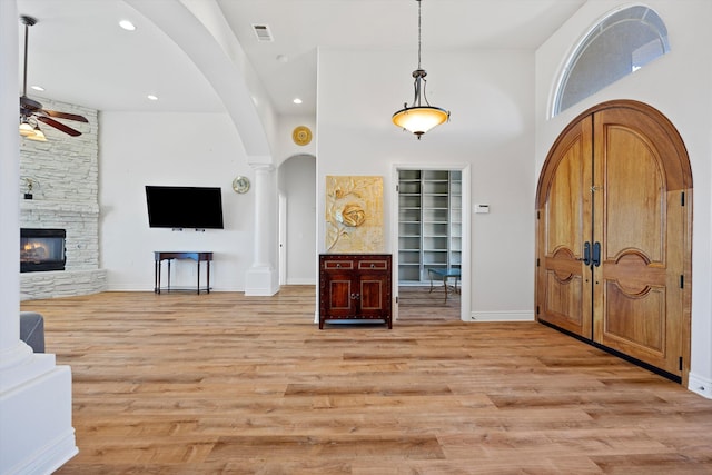 entrance foyer with a high ceiling, light wood-type flooring, a stone fireplace, and ceiling fan