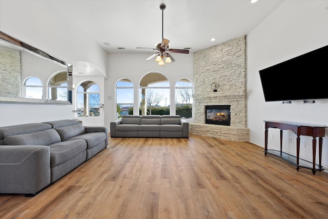 living room featuring a stone fireplace, ceiling fan, and light hardwood / wood-style floors