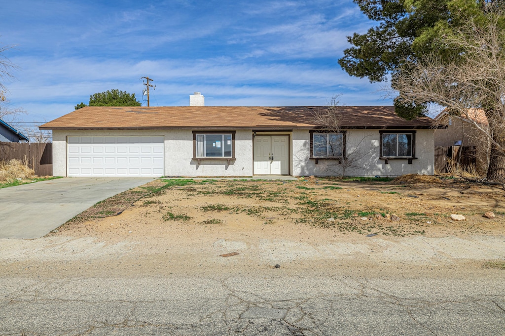 single story home featuring an attached garage, fence, concrete driveway, stucco siding, and a chimney