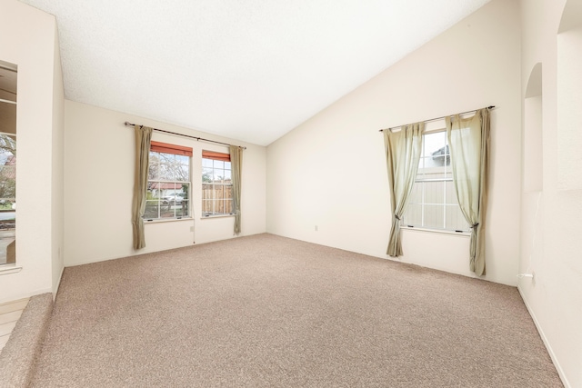 carpeted spare room with vaulted ceiling and arched walkways