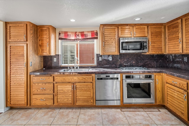 kitchen with light tile patterned flooring, appliances with stainless steel finishes, tasteful backsplash, sink, and a textured ceiling