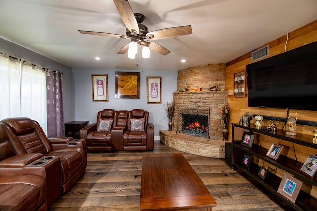living room with a ceiling fan, a stone fireplace, visible vents, and dark wood-style flooring