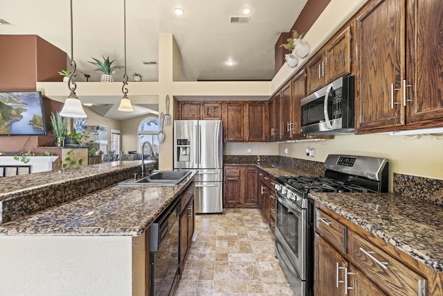 kitchen with appliances with stainless steel finishes, decorative light fixtures, sink, dark stone counters, and a kitchen island with sink