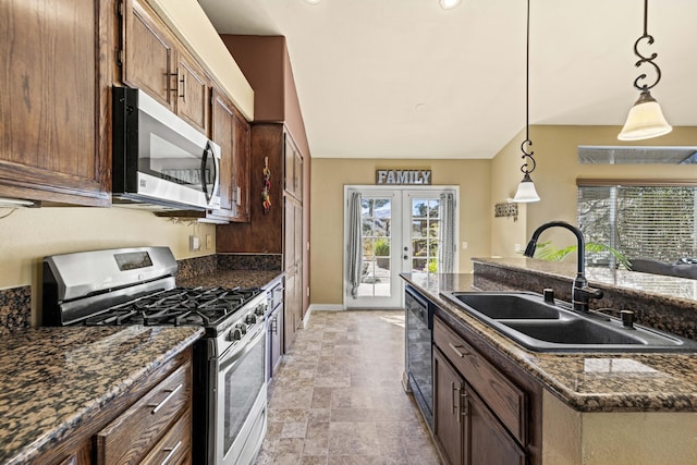 kitchen with appliances with stainless steel finishes, hanging light fixtures, sink, french doors, and dark stone counters