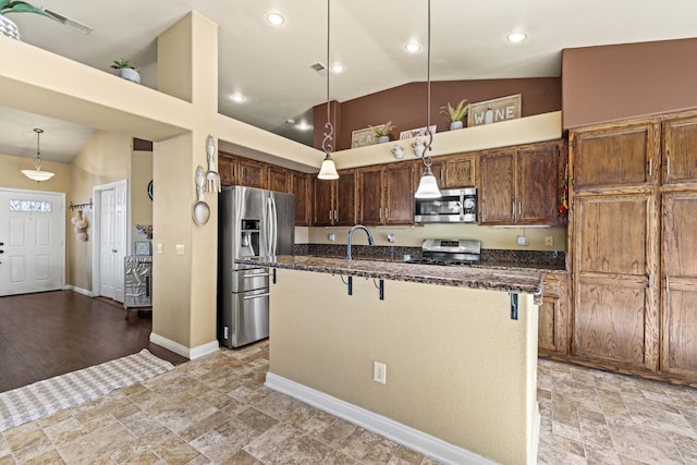 kitchen with appliances with stainless steel finishes, a kitchen bar, hanging light fixtures, a kitchen island with sink, and vaulted ceiling